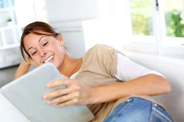 young woman using electronic tablet laying on sofa