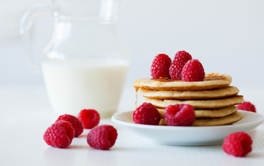 Pile of pancakes with raspberries and jug of milk