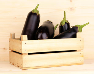Fresh eggplants in crate on wooden background