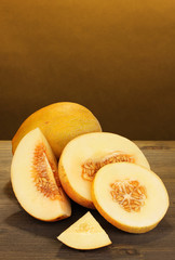 Cut ripe melons on wooden table on orange background