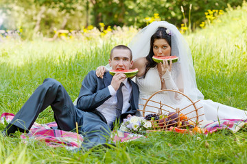 groom with  bride sit on a grass and eat a juicy water-melon