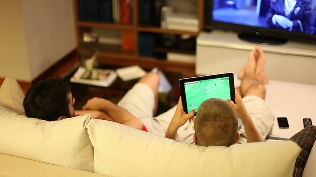 Boys on sofa watching tv and playing with tablet