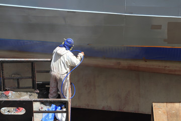 worker painting ship hull using airbrush gray paint