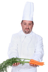 Chef in uniform with a bunch of fresh carrots