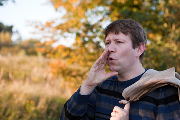 Young man  shouting in autumn forest on sunny day