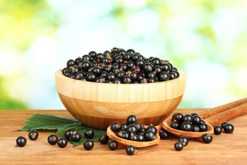 Fresh black currant in wooden bowl on green background close-up