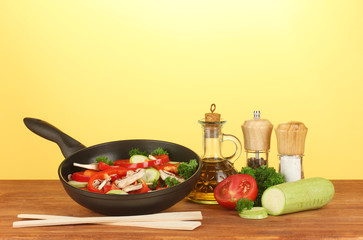 frying pan with vegetables on yellow background