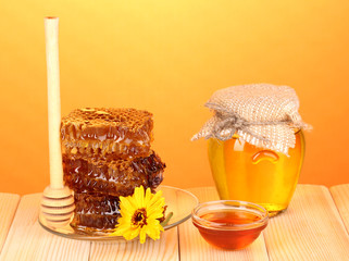 Jar of honey and honeycomb on wooden table on orange background