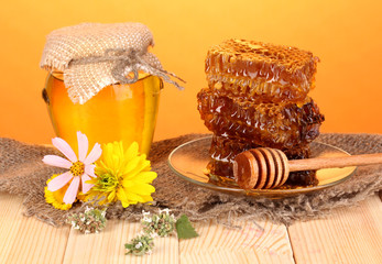 Jar of honey and honeycomb on wooden table on orange background