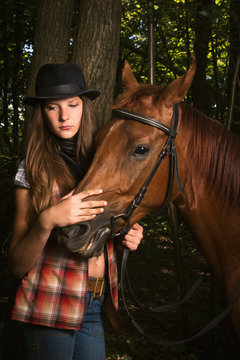 Cowgirl in hat with bay horse