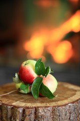Jabłka na gałązce z liśćmi na drewnianym pniu, na tle płonącego kominka. © Stanisław Błachowicz