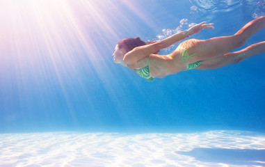 Woman swimming underwater in a blue pool.