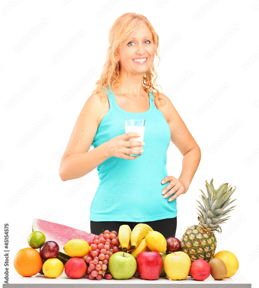 Sticker Woman holding a glass of milk with pile of fruits on a table