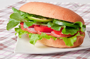 Sandwich with ham, tomato, cucumber and arugula on the white pla