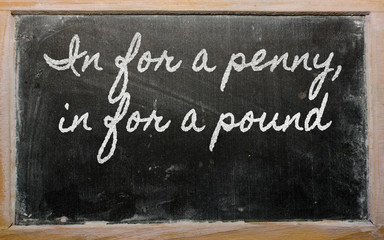 expression -  In for a penny, in for a pound - written on a scho