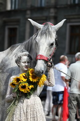 Dziewczyna pomalowana gliną trzyma w ręku oęk słoneczników i siwego konia za uzdę, glinoludy w Bolesławcu. © Stanisław Błachowicz