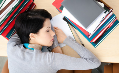 Female student sleeping at the desk with piles of books