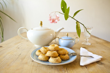 a plate of biscuits, a tea pot and a flower on wooden table