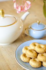 a plate of biscuits, a tea pot and a flower on wooden table