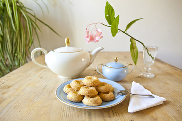 a plate of biscuits, a tea pot and a flower on wooden table