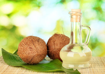decanter with coconut oil and coconuts on green background