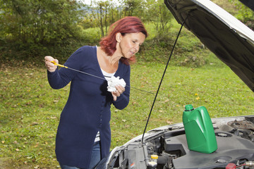 Cute woman checking level of oil on a car engine dipstick