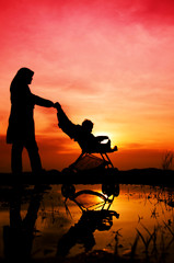 Fototapeta na wymiar Muslim matki i dziecka chodzenia podczas zachodu słońca z wózka.
