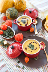 Zwei kleine rote Töpfe mit Deckel mit Kürbissuppe, Kürbiskernen 