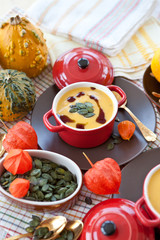 Zwei kleine rote Töpfe mit Deckel mit Kürbissuppe, Kürbiskernen 