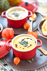 Zwei kleine rote Töpfe mit Deckel mit Kürbissuppe, Kürbiskernen 