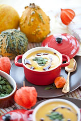 Zwei kleine rote Töpfe mit Deckel mit Kürbissuppe, Kürbiskernen 