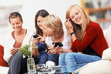 4 girls with smartphones on the sofa