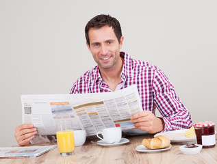 Young Man Reading Newspaper At Breakfast