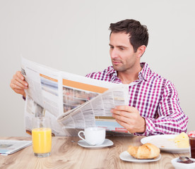 Young Man Reading Newspaper At Breakfast