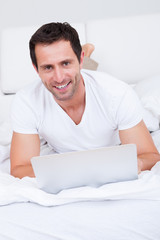 Portrait Of Young Man Lying On Bed Using Laptop