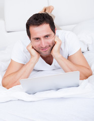 Portrait Of Young Man Lying On Bed Using Laptop