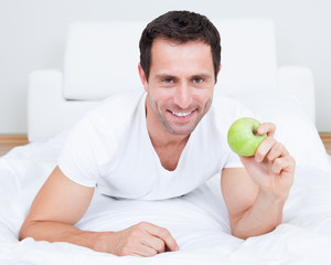 Young Man Lying On Bed Holding Green Apple