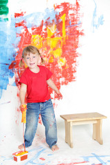 young happy child girl painting white wall with colours