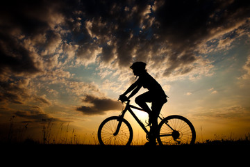 Fototapeta na wymiar Biker-girl at the sunset on the meadow