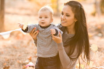 Happy mother and son with pumpkin on autumn leaves. Outdoor.