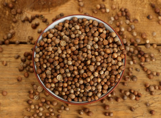 Heap coriander seeds in bowl on wooden background close-up