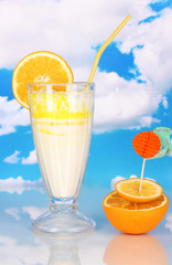 Delicious milk shake with orange on table on sky background