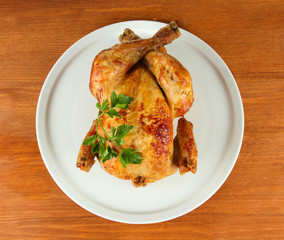 Roasted whole chicken on a white plate on wooden background