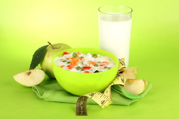 tasty dieting food and glass of milk, on green background