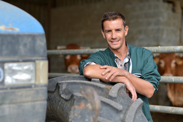 Obraz premium Handsome farmer leaning in barn on tractor wheel