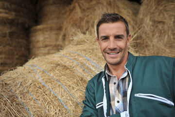 Portrait of cheerful farmer standing in front of hay rolls © goodluz