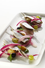 Sardines with grapes and red onion on white plate