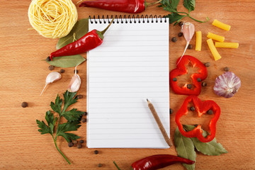 notebook for recipes, vegetables and spices on wooden table.