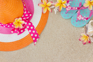 Hat and Flip Flops in the sand with shells and frangipani flower