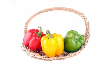 three colorful peppers in a straw basket, isolated on white